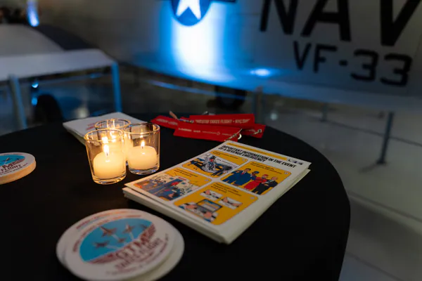 Candles, event coasters and a printed programme on a cocktail table beneath a Navy jet.