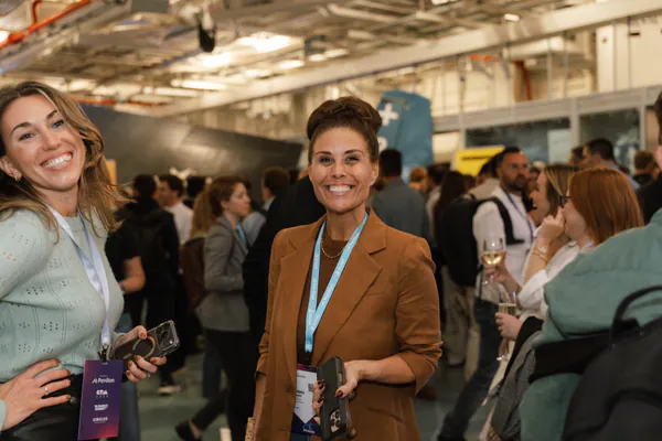 Two guests with lanyards smile at the camera in the busy hangar.