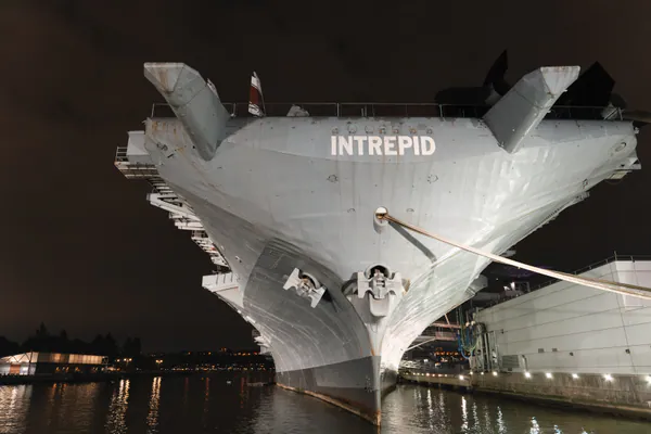The bow of the aircraft carrier Intrepid, lit up at night on the Hudson.